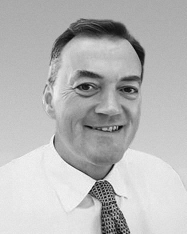 Black-and-white corporate headshot of a man wearing a shirt and patterned tie. {{brizy_dc_image_alt imageSrc=