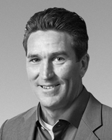 Black-and-white professional portrait of a man wearing a suit jacket and shirt. {{brizy_dc_image_alt imageSrc=