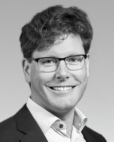 Black-and-white professional headshot of a man wearing glasses, blazer and shirt. {{brizy_dc_image_alt imageSrc=